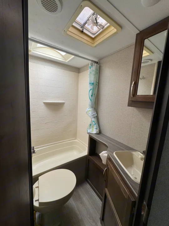 This RV rental bathroom features a compact tub/shower, toilet, sink vanity, and skylight for bright, comfortable use.. Dutchmen Coleman Light 2019