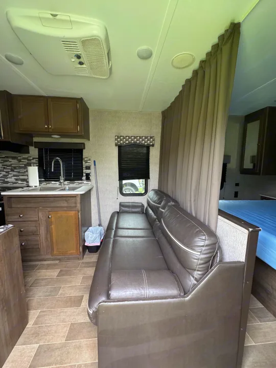 Explore this rv rental interior, featuring a functional kitchenette, convertible sofa, ceiling AC unit, and private bed area.. Dutchmen Coleman Lantern LT 2020
