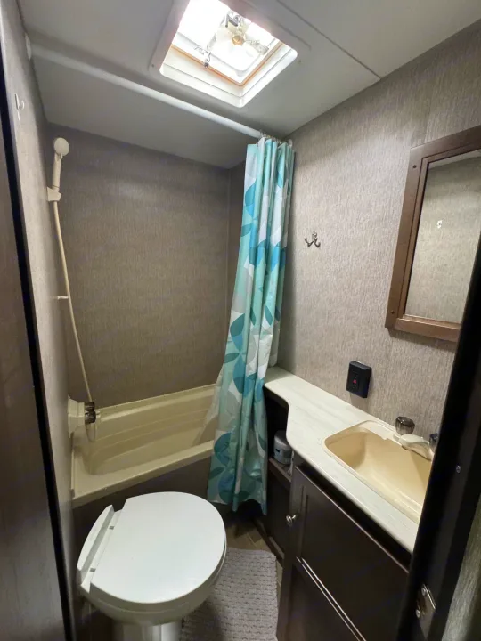 Compact RV rental bathroom with toilet, shower, sink, mirror, and ceiling skylight, designed for efficient travel.. Dutchmen Coleman Lantern LT 2020