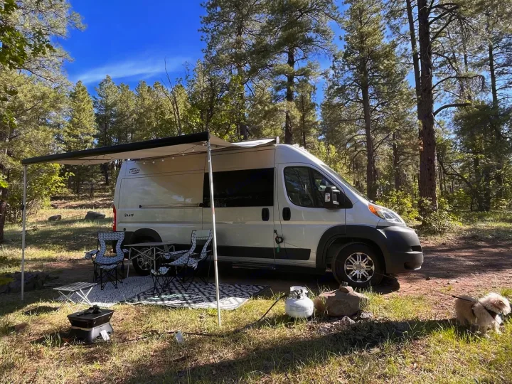 This RV rental camper van is set up for a campsite adventure with an awning, chairs, fire pit, and a dog.. Hymer Carado 2018