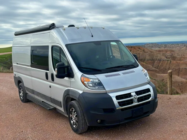 Silver RV rental van parked on a dirt road overlooking the rugged Badlands National Park landscape under cloudy skies.. Hymer Carado 2018