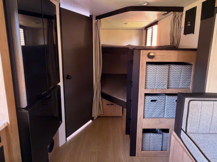 Interior of an rv rental with bunk beds, storage bins, and a dinette area, showcasing a compact and functional living space.. Forest River Campsite Reserve 2026