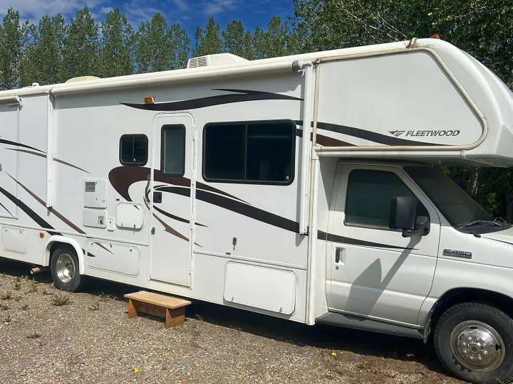 White Fleetwood E-450 RV rental parked on gravel with trees. A wooden step stool is by the main entrance.. Tioga Montara 2013
