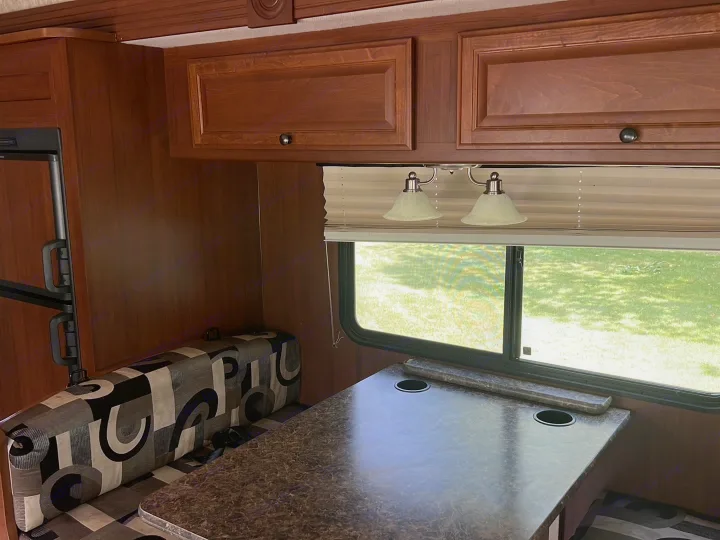 Cozy RV rental interior: a dining booth with patterned cushions, a table with cupholders, overhead cabinets, and a green window view.. Tioga Montara 2013