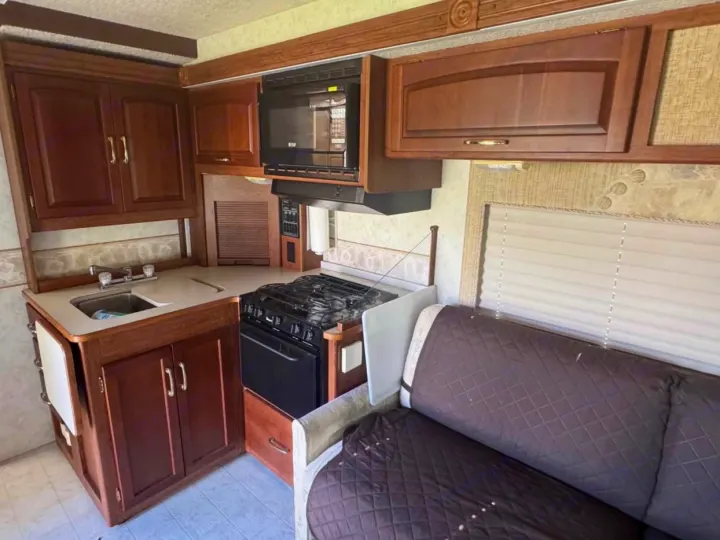 RV rental interior: functional kitchen with wood cabinets, stove, microwave, sink, and a cozy sofa with quilted cover.. Winnebago Itasca 2001