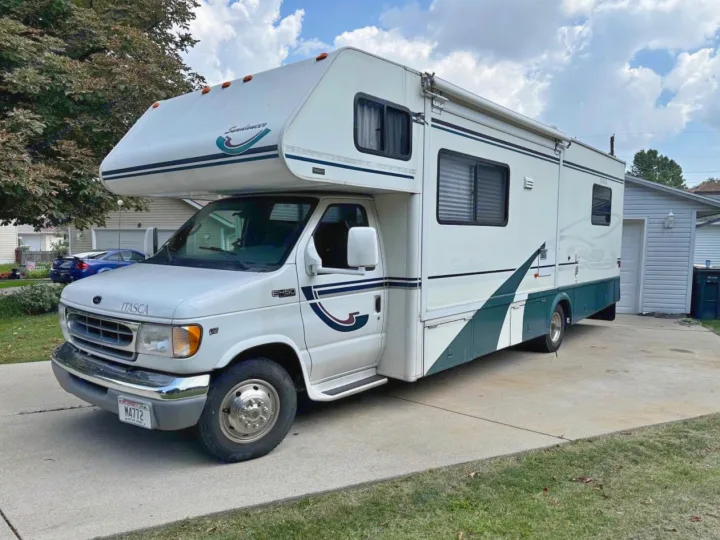 White Class C motorhome, an rv rental, with teal accents, parked on a paved driveway, ready for adventure.. Winnebago Itasca 2001