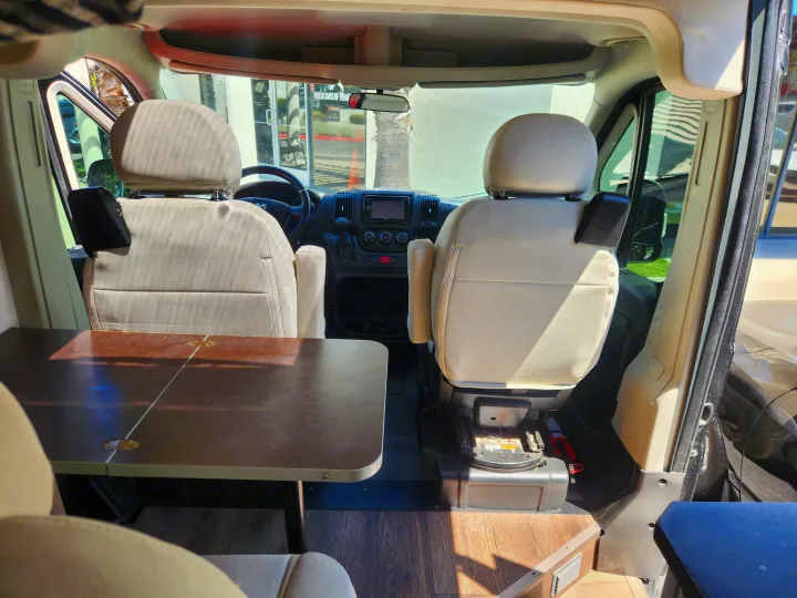 RV rental: View inside a camper van showing front swivel seats, a table, and the dashboard. A car dealership is seen outside.. RAM ProMaster 3500 2016