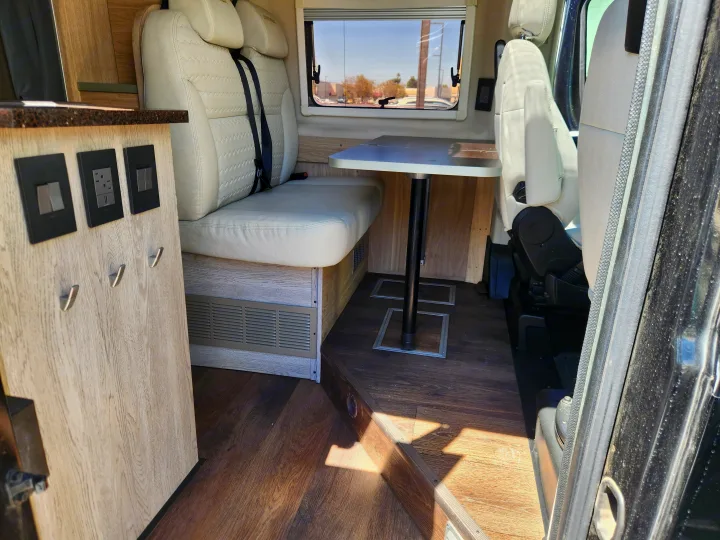 Inside an rv rental: A modern campervan dinette with plush seating, convenient power access, and wood-look finishes.. RAM ProMaster 3500 2016