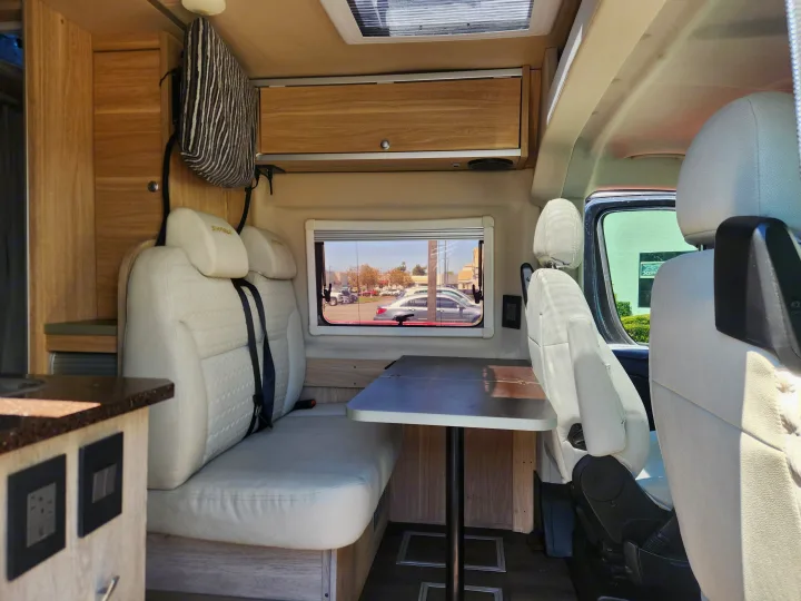 Cozy rv rental interior featuring a dining area with white seating, a table, and light wood cabinets.. RAM ProMaster 3500 2016
