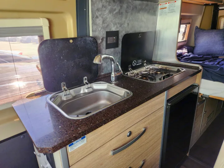 This RV rental's efficient kitchenette features a sink, 2-burner stove, and fridge, ideal for travelers.. RAM ProMaster 3500 2016