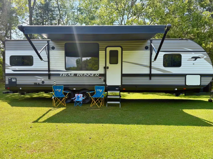 RV rental ready for adventure: a Trail Runner travel trailer with awning, chairs, and cooler on a sunny campsite.. Heartland RVs Trail Runner 2022