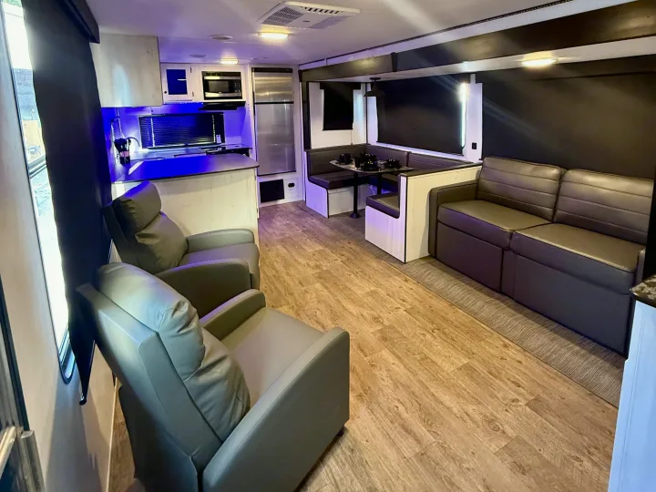 Spacious RV rental interior features a modern kitchen with blue lighting, a dining booth, and comfortable living area seating.. Heartland RVs Trail Runner 2022