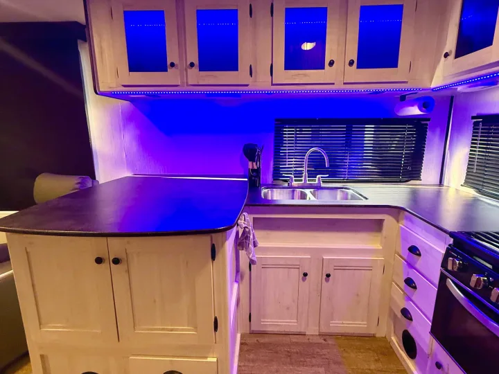 Brightly lit RV rental kitchen featuring blue LEDs, light cabinets, a double sink, and sleek countertop for your travels.. Heartland RVs Trail Runner 2022