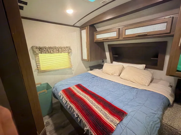 Cozy RV rental bedroom with a comfortable bed, overhead storage, and window, perfect for your travel.. Keystone RV Cougar 2019