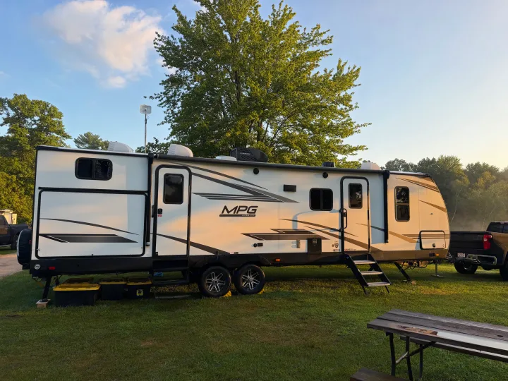 White MPG travel trailer rv rental parked on a grassy site. A portable satellite dish is visible, along with a picnic table.. Cruiser RV MPG Ultra Lite 2022