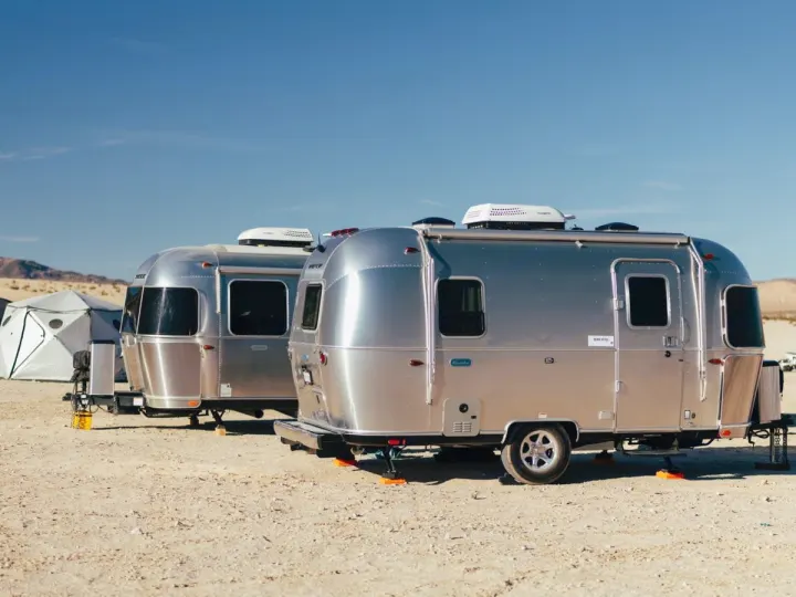 Two shiny silver RV rental travel trailers and a modern tent parked on a sandy desert floor under a clear blue sky.. Airstream Bambi 2023