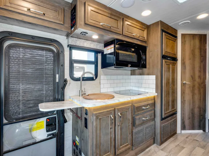 RV rental: compact kitchen with wood-grain cabinets, microwave, sink, stovetop, fridge, and screen door.. Jayco Melbourne 2022