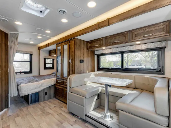 Cozy RV rental interior featuring a U-shaped dining booth, bed, and modern wood accents, with bright natural light.. Jayco Melbourne 2022