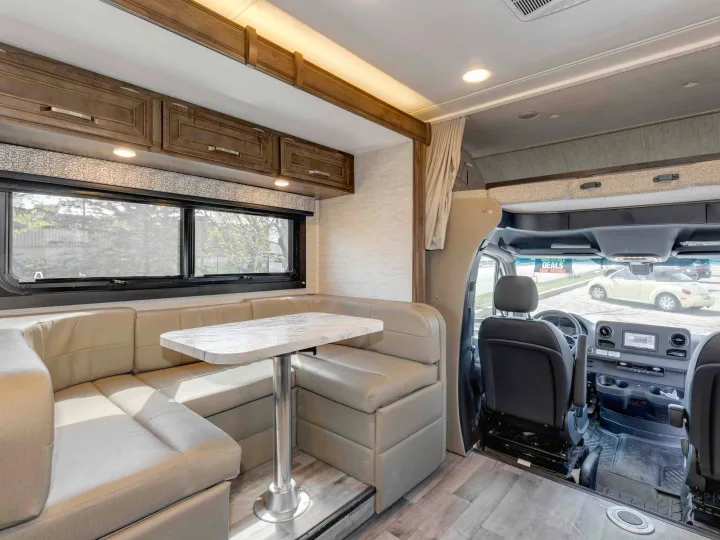 Comfortable RV rental interior with light-colored U-shaped dinette, dining table, overhead storage, and view to the driver's cabin.. Jayco Melbourne 2022