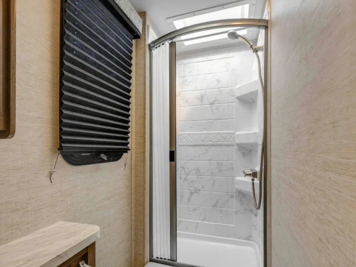 RV rental bathroom featuring a bright shower with a skylight, marble-look walls, and a black pleated blind.. Jayco Melbourne 2022