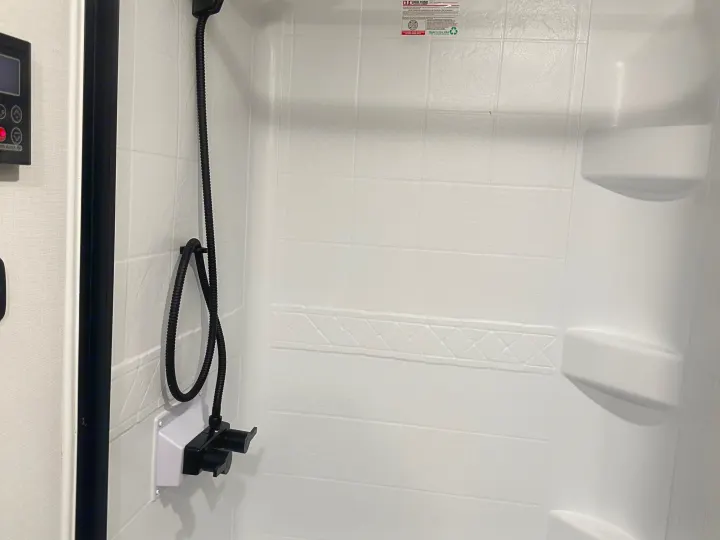 Inside an RV rental shower: white molded walls, handheld shower, black water controls, and built-in shelves.. Keystone RV Passport SL 2025