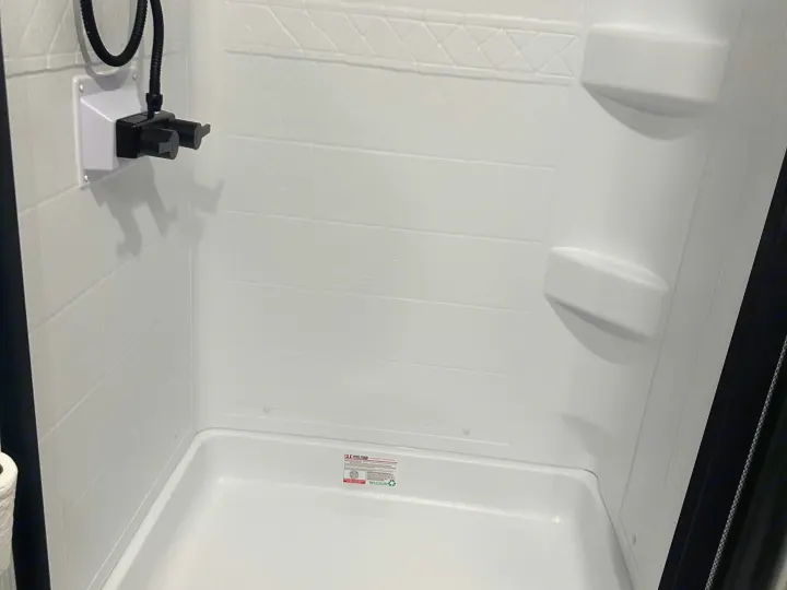 RV rental shower: white, compact, featuring textured walls, a built-in shelf, and black shower controls.. Keystone RV Passport SL 2025