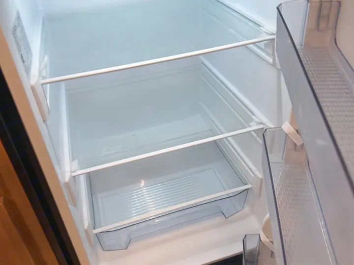 Inside a clean, empty RV rental mini-fridge, featuring wire shelves and a crisper drawer, ready for your trip.. Keystone RV Passport SL 2025