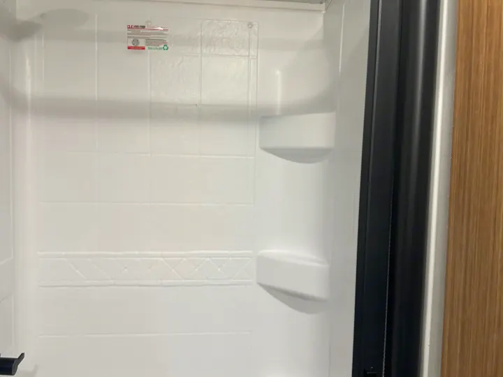 This RV rental features a clean white shower with molded tile texture, convenient built-in shelves, and dark trim.. Keystone RV Passport SL 2025