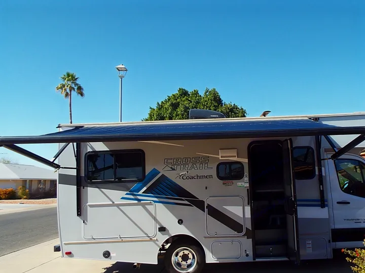 Coachmen CROSS TRAIL RV rental, grey, with extended awning & open door, parked under clear sky with palm tree.. Coachmen Ford Transit 2023