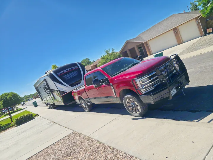 A powerful red pickup truck is seen towing a large Stryker RV, parked curbside. Consider this setup for your next rv rental adventure!. Cruiser Rv Corp Stryker 2025