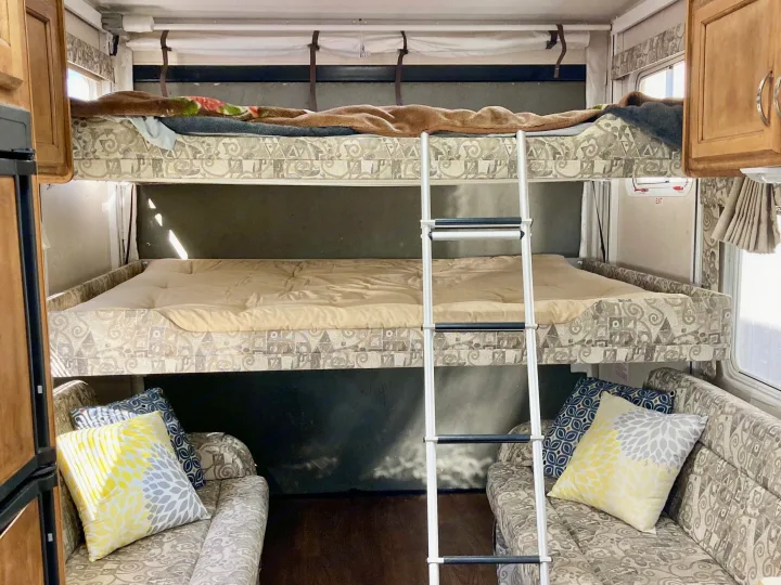 Spacious RV rental interior featuring comfortable bunk beds, a ladder, and twin seating areas with colorful pillows.. Rage'N Toy Hauler 2006
