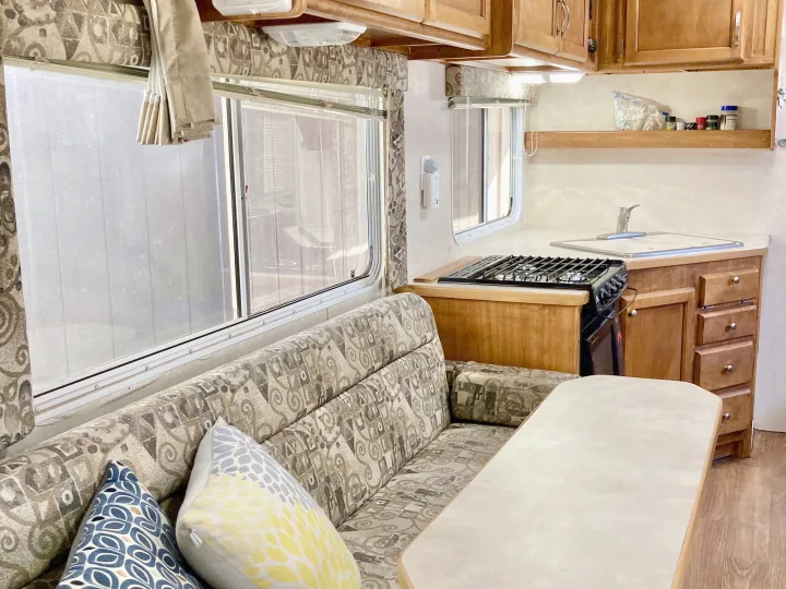 This rv rental features a cozy dinette with patterned sofa seating, a dining table, and a compact kitchen including a stove and sink.. Rage'N Toy Hauler 2006