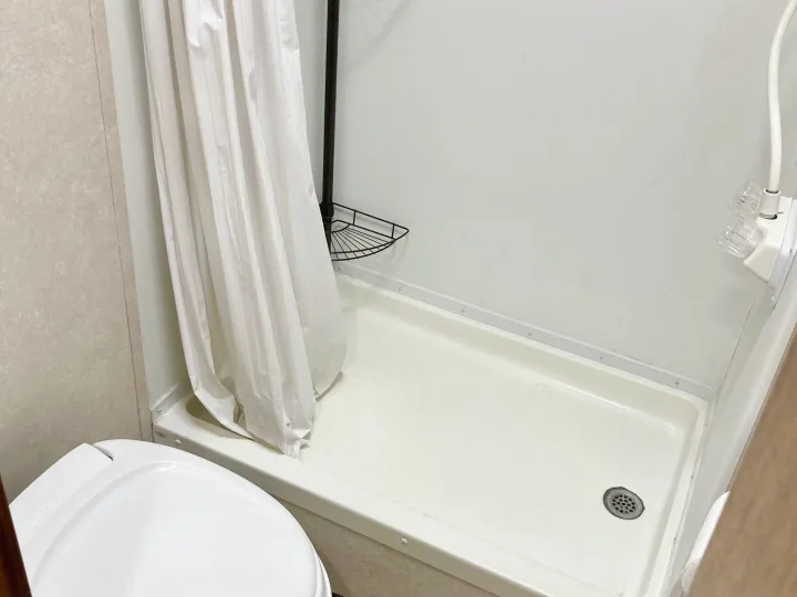 Compact RV rental bathroom featuring a white shower with curtain, corner storage, and part of the toilet.. Rage'N Toy Hauler 2006