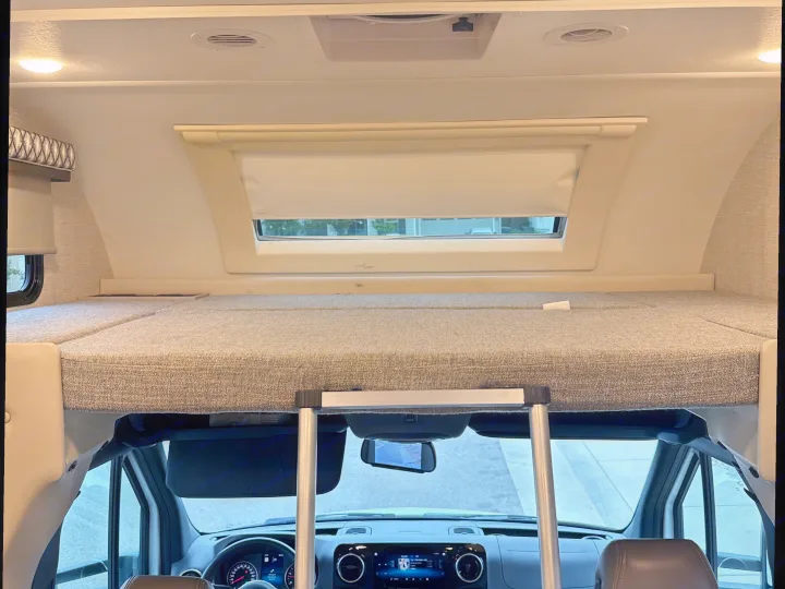 RV rental interior: Cab-over bunk bed with a ladder, overhead lights, and a view of the road from the driver's area.. Thor Quantum 2023