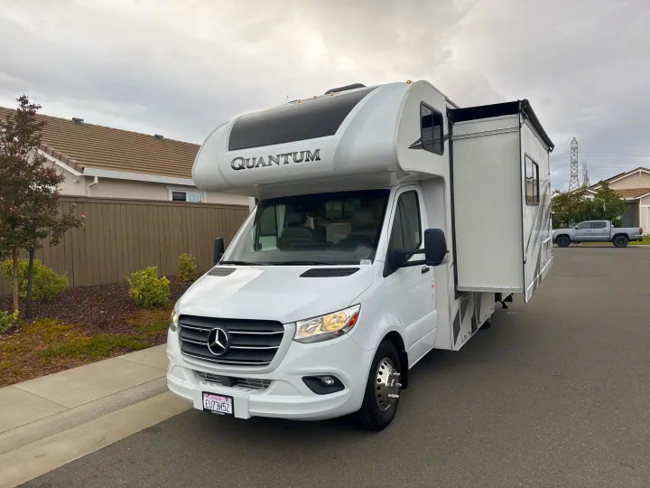 White Mercedes-Benz Quantum rv rental, with its slide-out extended, parked on a street.. Thor Quantum 2023