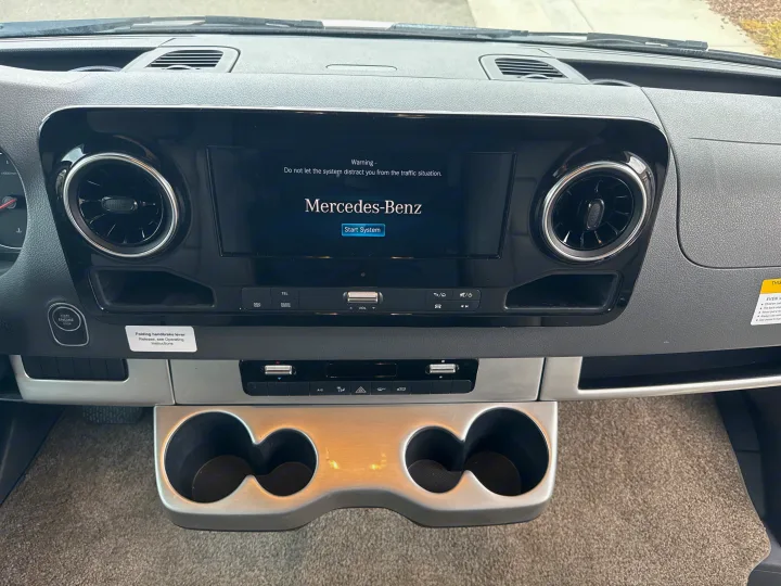 Mercedes-Benz RV rental dashboard, showing infotainment screen with safety warning, air vents, start button, and cup holders.. Thor Quantum 2023
