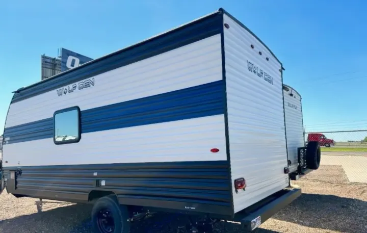 White and blue "Wolf Den" travel trailer, available for RV rental, with a spare tire on back. Great for camping trips!. Forest River Cherokee Wolf Den 2024