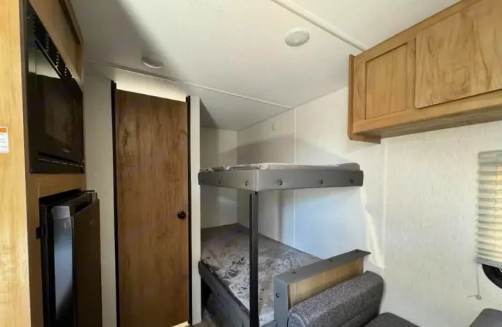 Cozy RV rental interior with stacked bunk beds, microwave, fridge, and wood cabinetry. Ideal for family adventures!. Forest River Cherokee Wolf Den 2024