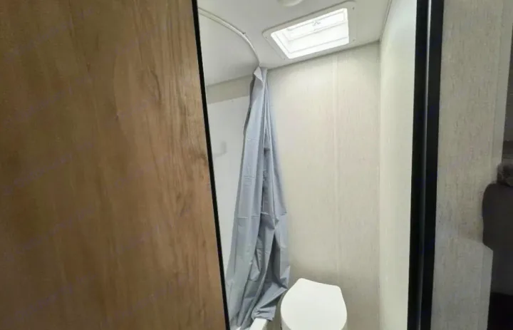 Compact rv rental bathroom featuring a toilet, shower curtain, and a skylight for natural light.. Forest River Cherokee Wolf Den 2024