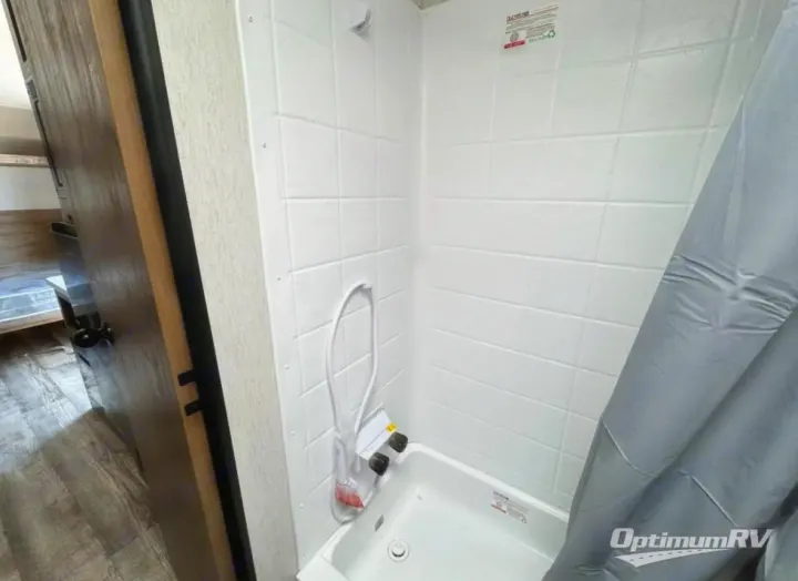 Experience comfort in this rv rental's clean white shower stall, complete with a handheld showerhead and grey curtain. Ideal for travel.. Forest River Cherokee Wolf Den 2024