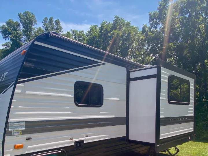 This RV rental, a white and black travel trailer with an extended slide-out, is parked outside with a generator running.. Keystone RV Hideout 2022