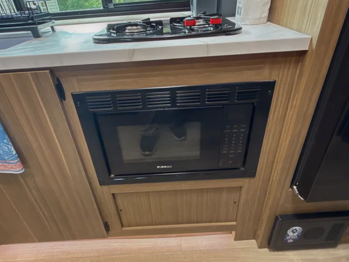 Compact RV rental kitchen with Furrion microwave, two-burner stovetop, and white countertop. Reflection of shoes visible.. Forest River Salem 2026