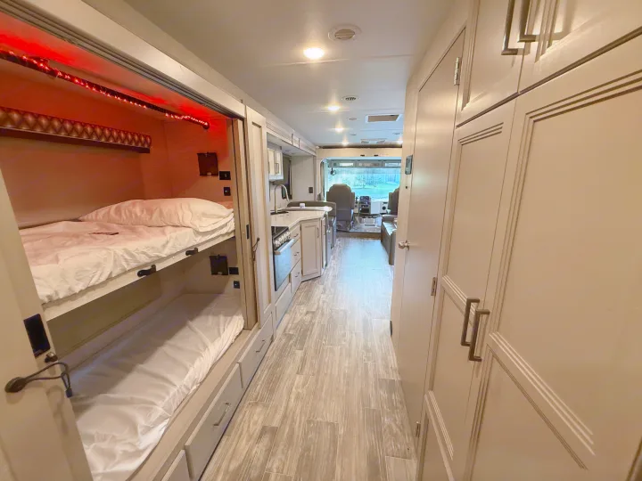 RV rental interior showcasing bunk beds with red LEDs, a modern kitchen, and the driver's cabin view ahead.. Thor Hurricane 2022