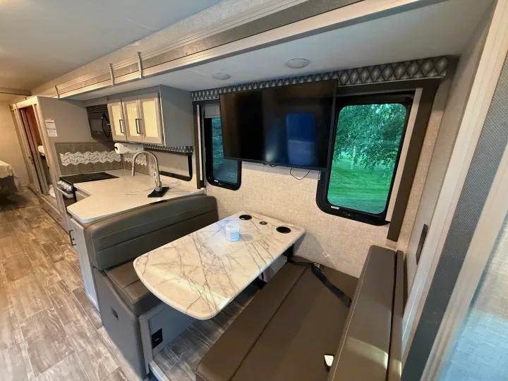 Modern rv rental interior showcasing a full kitchen, comfortable dinette with TV, and scenic window views for your travels.. Thor Hurricane 2022