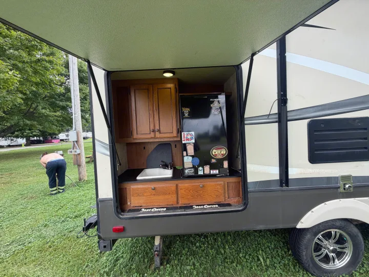 This RV rental's exterior kitchen boasts a mini-fridge, sink, and wood cabinets, with "Jose Cuervo" mats, perfect for camping.. Crossroads RV Sunset Trail Super Lite 2015
