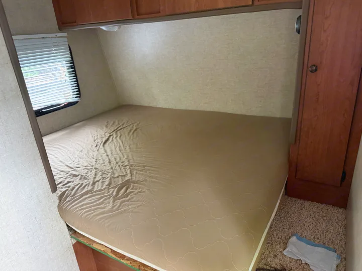 Compact RV rental bedroom with a bed, overhead wood cabinets, and a window with white blinds.. Sportsmen Classic 2013
