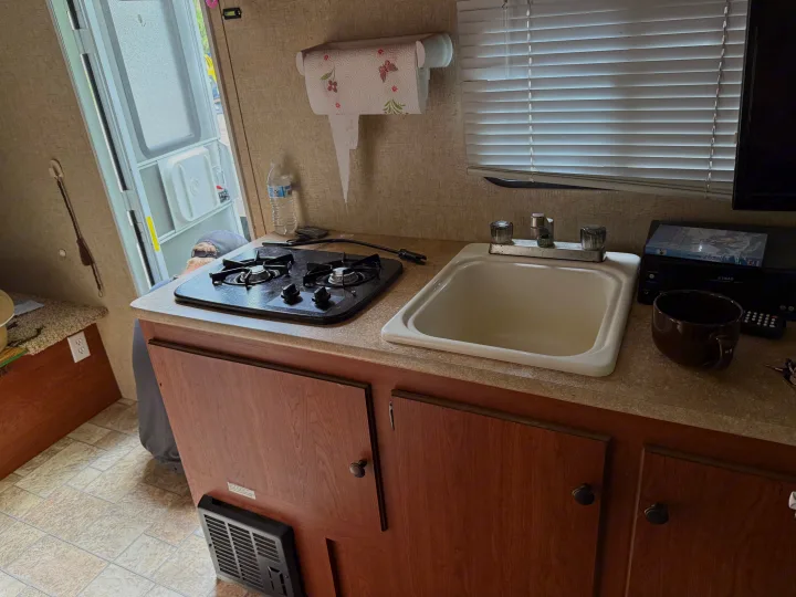 RV rental kitchen: stove, sink, paper towels, and view outside. Compact and functional design.. Sportsmen Classic 2013