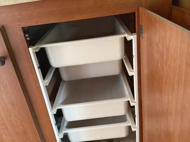 RV rental storage: Wood cabinet interior showcasing multiple stacked pull-out plastic bins on white metal frames.. Sportsmen Classic 2013