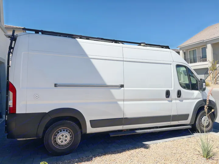 White RV rental conversion van with roof rack & side step, parked outside a home on a sunny day.. Dodge Ram 2500 2024