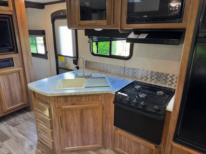 RV rental kitchen: light countertop, sink, gas stove, microwave, and wood-grain cabinets. Ready for your next adventure.. Jayco Jay Feather 2018
